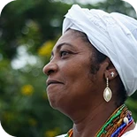 Woman wearing a head wrap outdoors, gently smiling.